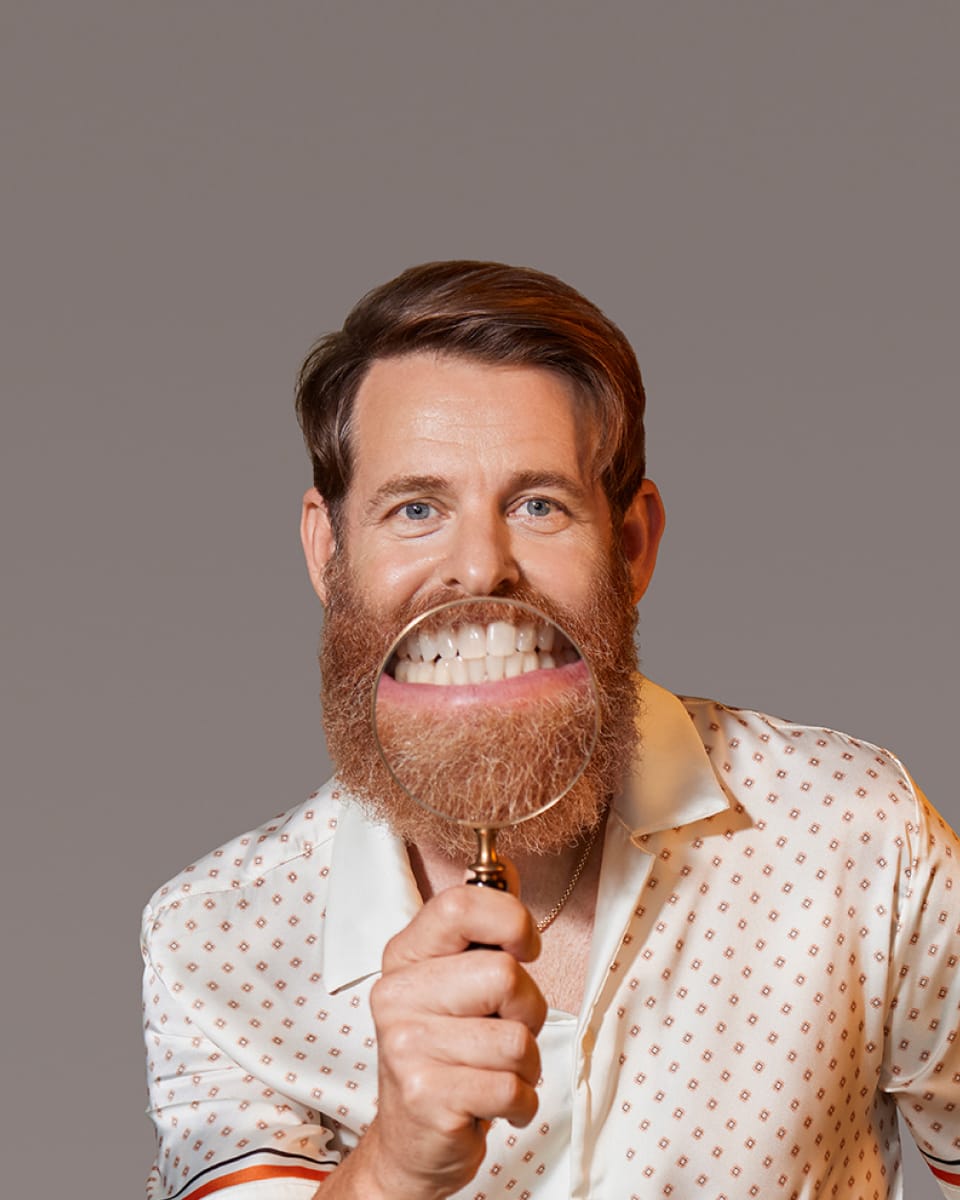 White male model holding up a magnifying glass to his beard